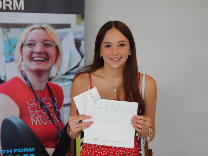 Proud female student holding up her results at results day