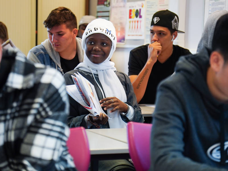 Student in classroom sat at desk holding maps.