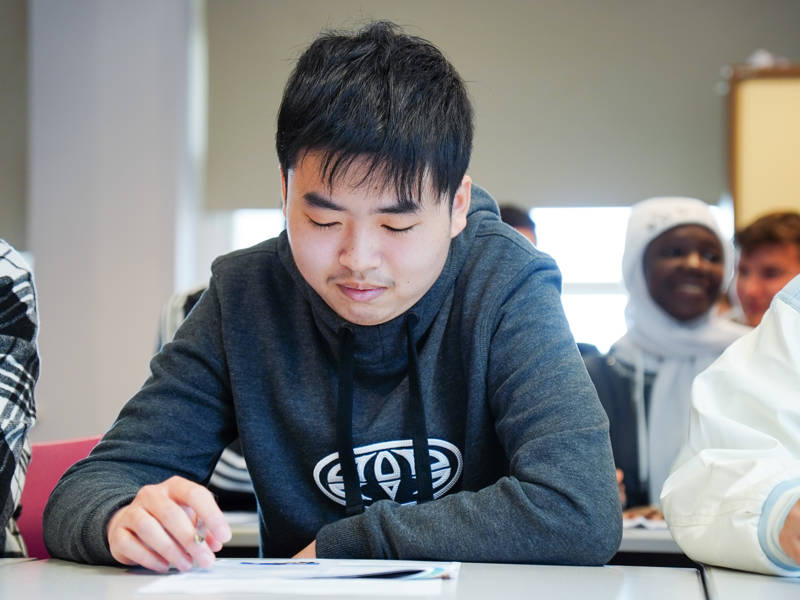 Student holding pen at desk focusing on work.