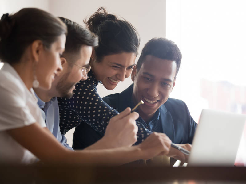 Smiling diverse employees have fun joking discussing ideas on computer at meeting.