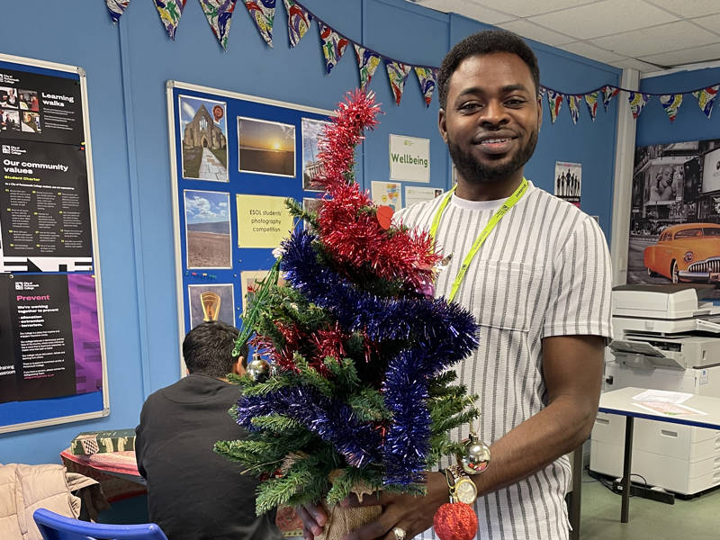Male ESOL student proudly holding decorated Christmas tree.