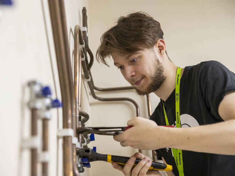 Plumbing student seen working on copper pipes.